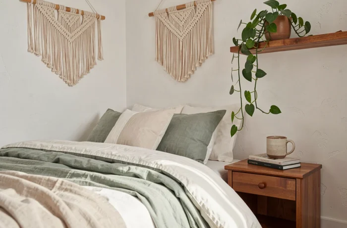 Coin chambre douillet avec literie en lin sauge et blanc, table de chevet en chêne et plante pothos sur étagère en bois